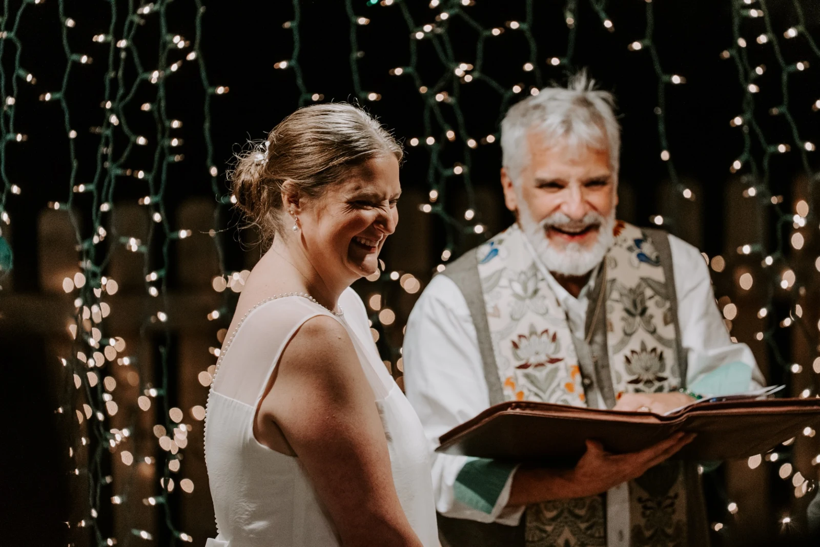 Kevin sharing a laugh with the bride while presiding at a wedding under string lights